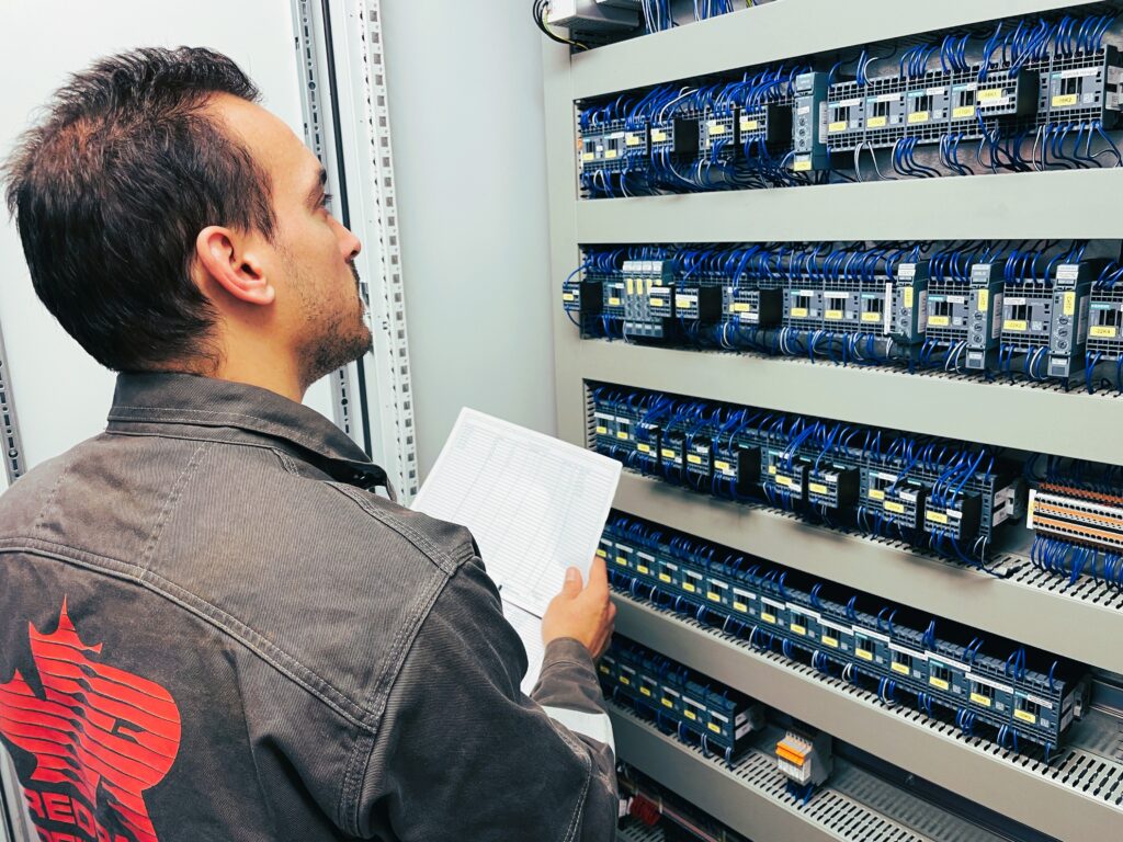 Mann mit einem Blatt in der Hand und Blick in einen Schaltschrank gerichtet