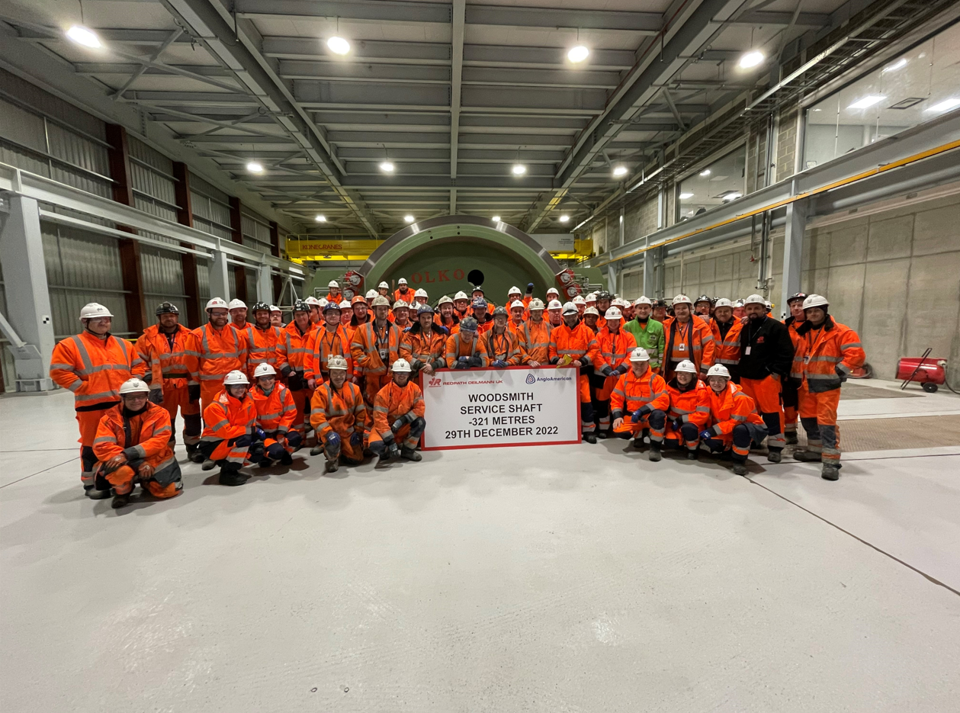 Gruppe von Menschen in orangener Arbeitskleidung in einer Halle