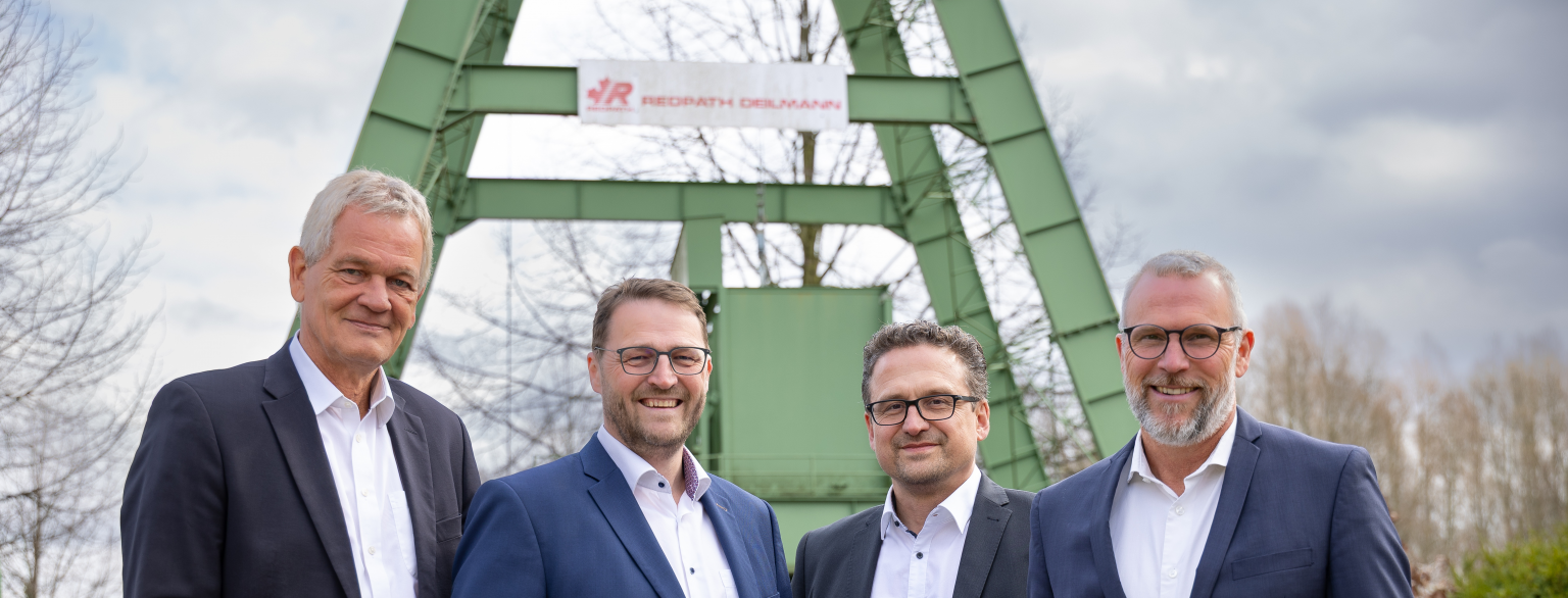 Gruppenfoto der Geschäftsleitung von REDPTAH DEILMANN vor dem Modell eines Förderturms - Jochen Greinacherm Dirk Thöne, Werner Siedentopf, Frank Otten